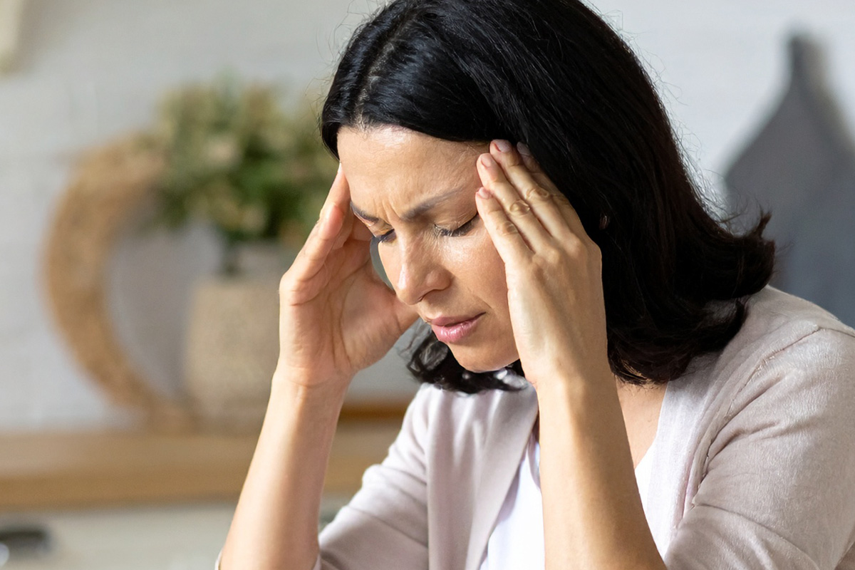 Stressed woman experiencing brain fog at home, holding head with both hands due to dehydration-related headache